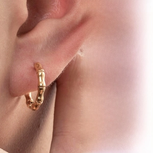 Close-up of gold bamboo-style hoop earring worn on ear with minimalist texture