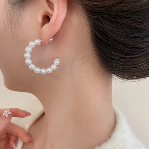 Close-up of elegant C-shaped pearl hoop earrings on model with soft lighting
