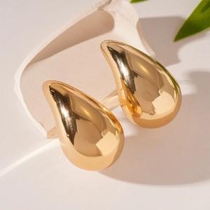 Close-up of golden teardrop earrings with a polished finish on a white decorative surface