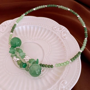 Detail of beaded green jade necklace with silver lotus charms on white porcelain