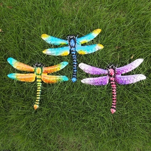 Three colorful metal dragonfly wall decorations with mesh wings displayed on green grass