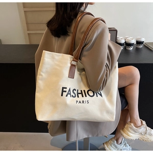 Detalle del bolso tote de lona crema con asas de cuero marrón y estampado de letras