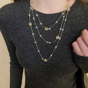 Three-layer gold chain necklace with amber crystal beads worn on a grey sweater