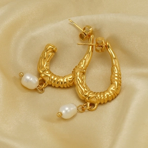 U-shaped stainless steel gold earrings with elegant pearl drops on silk background