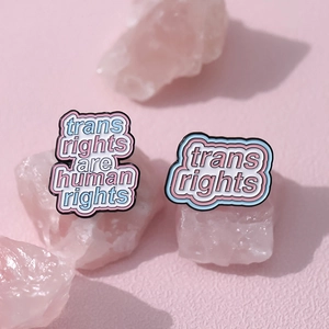 Trans Rights Are Human Rights enamel pins set on pink crystal with rainbow heart design