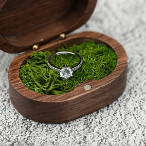 Macro shot of silver diamond ring with six-claw setting in walnut wood box and moss