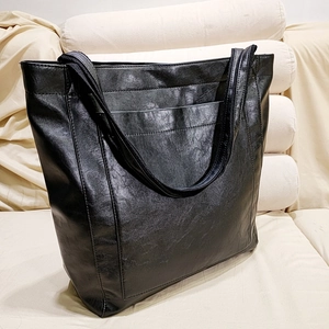Gros plan détaillé du sac cabas vintage en cuir huilé noir sur un canapé en tissu beige