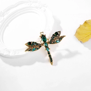 Macro view of vintage golden dragonfly brooch with emerald rhinestones and metal textures