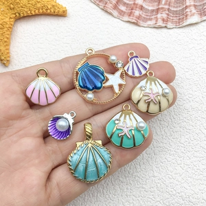 Enamel shell and starfish charms with pearls and rhinestones on a hand for scale