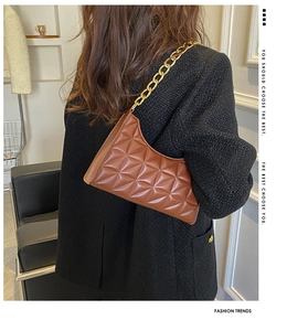 Close-up of brown quilted shoulder bag with chunky gold chain strap worn on-shoulder