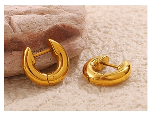 Detailed close-up of polished gold-plated hoop earrings on a natural stone surface