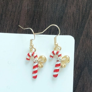 Detail of festive candy cane earrings with golden bows and rhinestones on wood backdrop