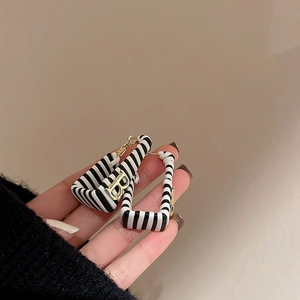 Detail of rectangular earring featuring black and white stripes with a gold-tone B initial