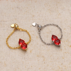 Detail of adjustable gold and silver chain rings with heart charms and red teardrop gems