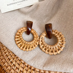 Detail of round woven straw earrings on fabric with vintage aesthetic and dark resin studs