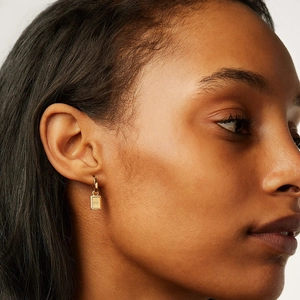 Macro detail of gold geometric rectangle earring with starburst engraving and zircon inlay