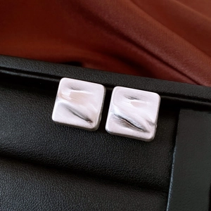 Gros plan de boucles d'oreilles carrées argentées avec texture ondulée brossée sur cuir