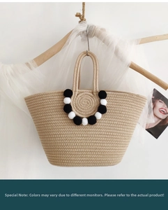 Detail of woven straw tote bag with black and white pom poms and textured pattern