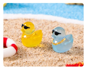 Close-up of yellow and blue miniature ducks with sunglasses and chains on a beach scene
