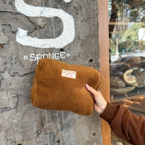 Close-up of brown faux shearling makeup bag with fabric patch in urban minimalist setting