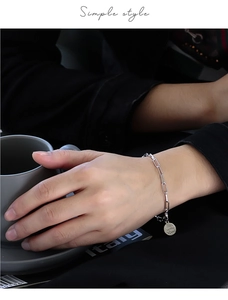 Detailed close-up of a silver paperclip link bracelet with a round charm on a wrist