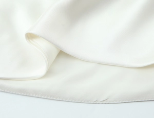 Detail view of the white satin shirt hem showing silky texture and fine stitching work