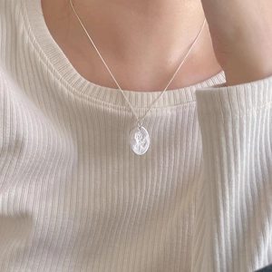 Detailed view of silver oval rose embossed pendant on a fine metal chain worn by a model