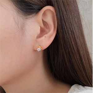 Detail of bow-shaped gold stud earring with round zircon on ear for a minimalist look