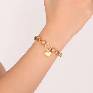 Close-up of gold heart pendant bracelet with matte beads worn on a model's wrist