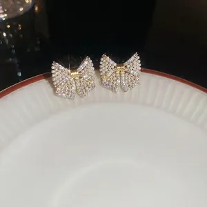 Sparkling silver needle bow earrings with pavé diamonds and pearls on a ceramic dish