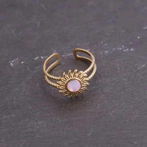 Détail d'une bague soleil dorée avec pierre rose sur roche sombre