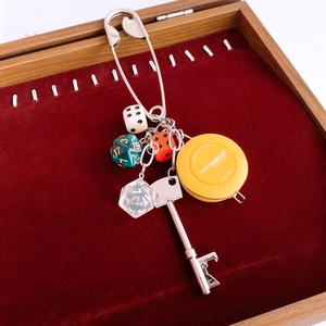 Detail of silver safety pin keychain with dice and yellow tape measure on red velvet