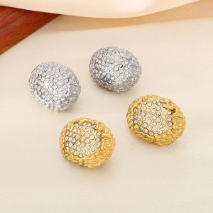 Close-up of gold and silver oval earrings with honeycomb texture and white rhinestones