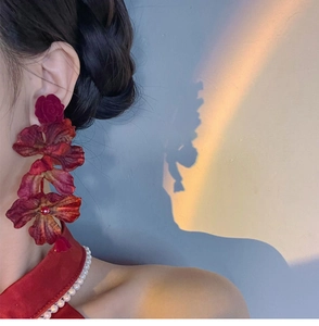 Close-up of elegant burgundy fabric rose earrings worn by a model in soft sunset lighting