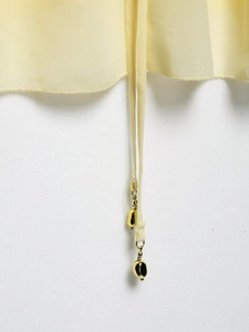 Détail du tissu en mousseline jaune clair avec perles dorées sur le cordon