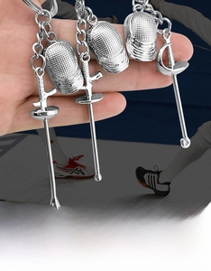 Detailed view of silver fencing mask and saber charms on a metal keychain