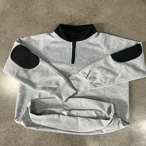Detail of grey quarter-zip sweatshirt showing black stand collar and elbow patches
