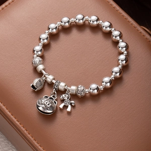 Detailed close-up of a silver beaded bracelet with bell and horse charms on leather