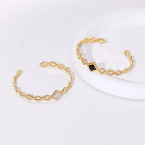 Detail of two gold geometric bangle bracelets with black and white diamond shaped accents