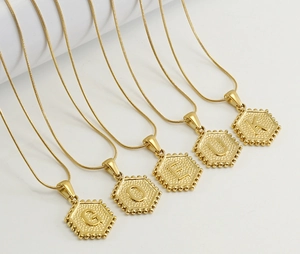 Détail de pendentifs hexagonaux en or 18k sur chaînes serpent avec lettres G O E U K