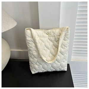 Detailed heart-quilted texture on beige tote bag with metallic snap button closure