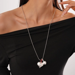 Close-up of a long ball chain necklace with silver heart, red bead, and polka dot charms