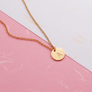 Gros plan d'un collier doré en acier inoxydable avec pendentif rond gravé de la lettre A