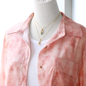 Close-up of a double-layered gold necklace featuring a colorful bird pendant on a model