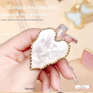 Close-up of heart-shaped white resin nail art ring palette with gold trim and marble texture