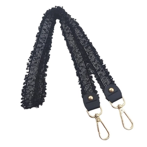 Black tweed bag strap with fringe edges and gold metal clasps on white background