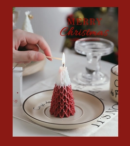 Close-up of hand lighting a red and white snow-topped Christmas tree candle