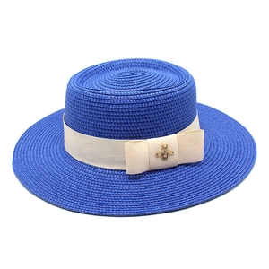 Close-up of bright blue straw boater hat featuring a cream ribbon and gold bee buckle