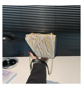 Detail of crossbody bag featuring brown and yellow wave patterns and metal chain strap