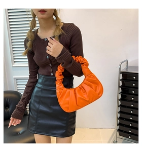 Fashionable orange pleated crescent bag worn by model in a stylish indoor setting